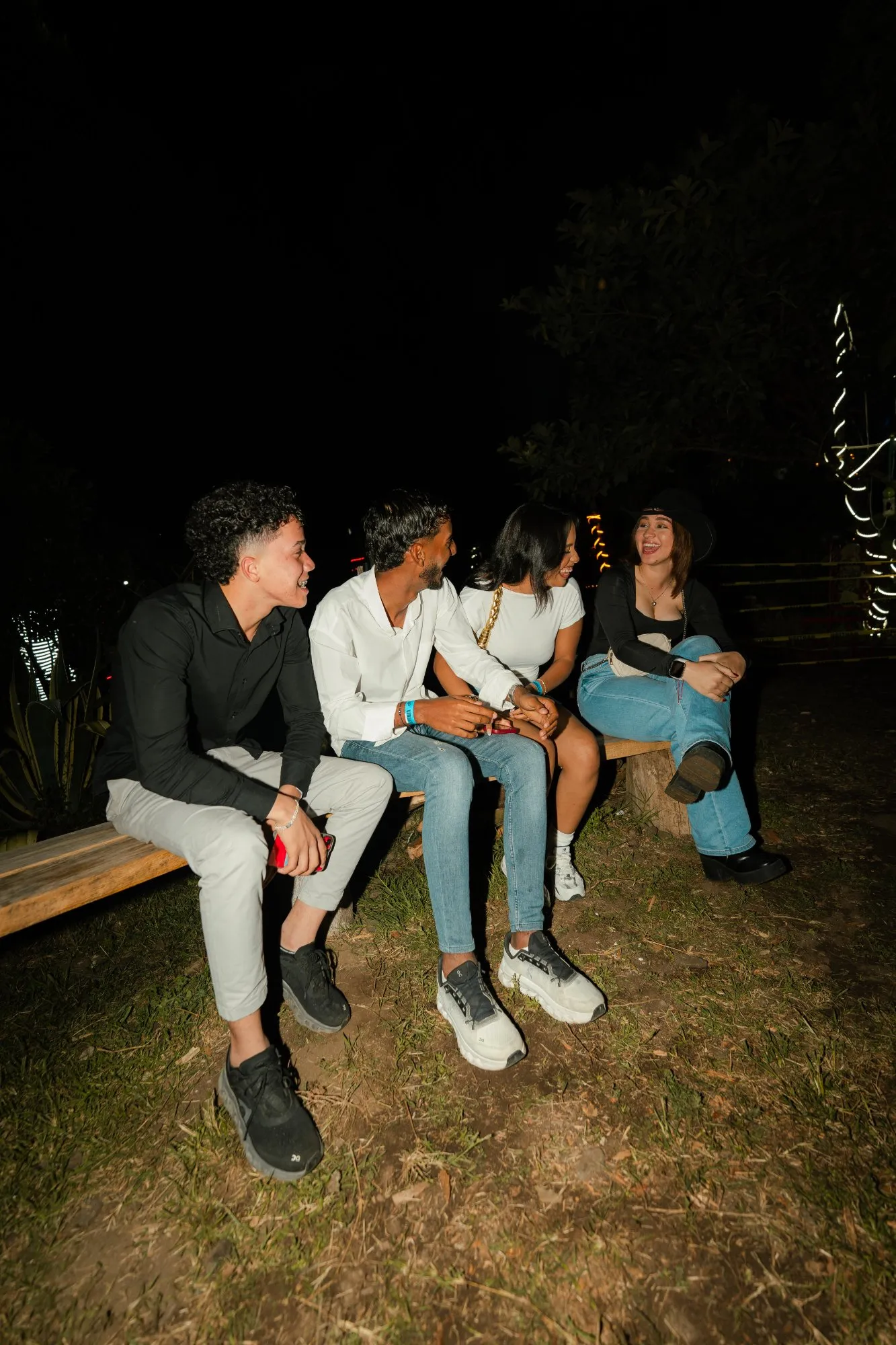Grupo de asistentes conversando en un banco de madera durante la noche